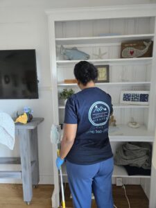 A house cleaner from Solange D Kleaner in New Bedford, MA, carefully dusting a bookshelf.