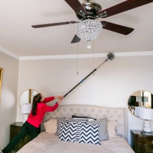 A house cleaner dusting a ceiling fan and molding in a bedroom with an extendable duster by New Image Cleaning Service LLC in Richmond, VA.
