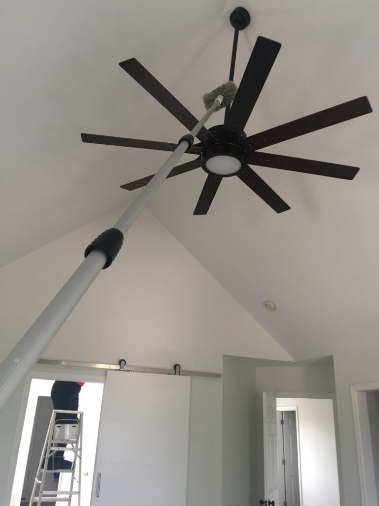 A house cleaner dusting a ceiling fan with an extendable duster for Wonderful Laura Cleaning in Aurora, IL.