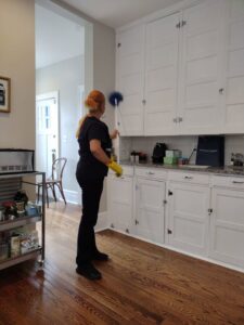 A house cleaner wearing gloves, dusting the top of kitchen cabinets for Creativity Cleaning LLC in Detroit, MI.