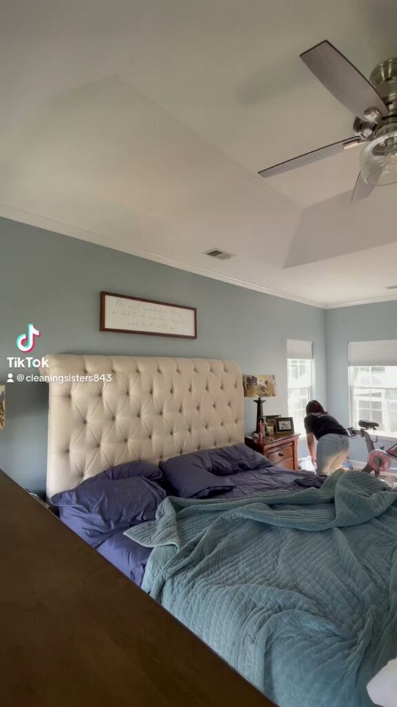 A house cleaner from Cleaning Sisters LLC in Richmond, VA, meticulously making a bed in a client's bedroom.