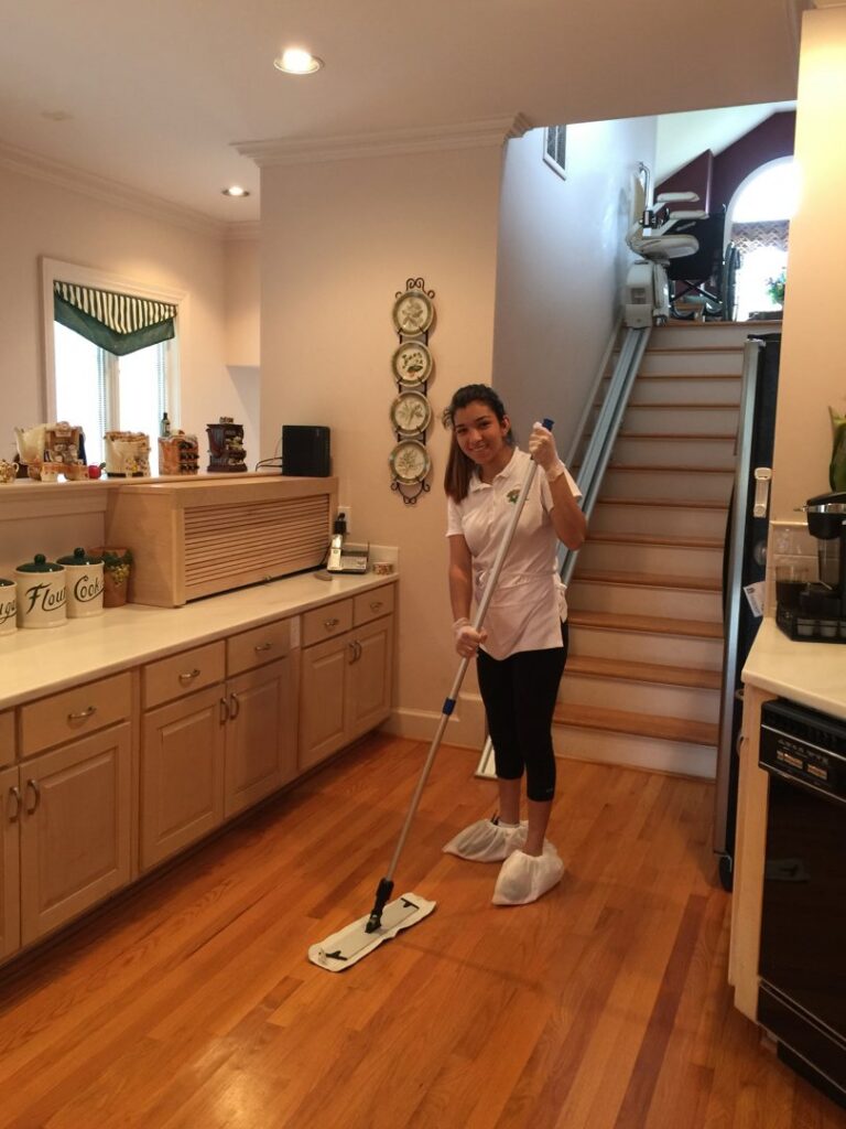 A house cleaner from Carolina Cleaning Services in Rocky Mount, NC, mopping a wooden kitchen floor with a flat mop.