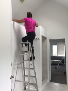 A house cleaner on a ladder cleaning a high surface in a home by Wonderful Laura Cleaning in Aurora, IL.