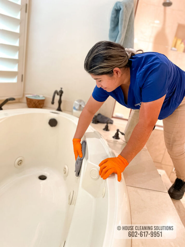 A house cleaner from House Cleaning Solutions in Mesa, AZ, is thoroughly scrubbing a bathtub.