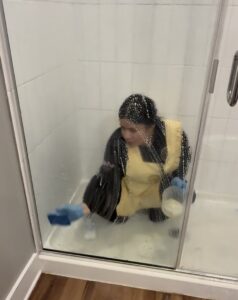 A house cleaner scrubbing a shower stall with a sponge and soap suds for Sunshine Cleaning & Painting in Raleigh, NC.