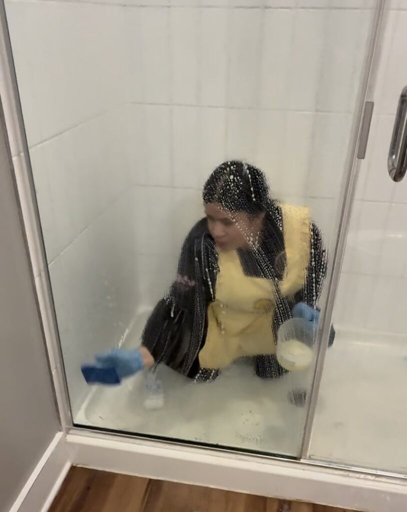 A house cleaner scrubbing a shower stall with a sponge and soap suds for Sunshine Cleaning & Painting in Raleigh, NC.