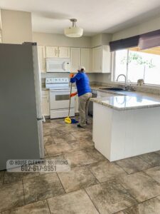 A house cleaner from House Cleaning Solutions in Mesa, AZ, is sweeping a kitchen floor with a broom.