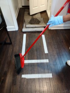 A house cleaner wearing gloves, sweeping a wooden floor with a broom for Creativity Cleaning LLC in Detroit, MI.