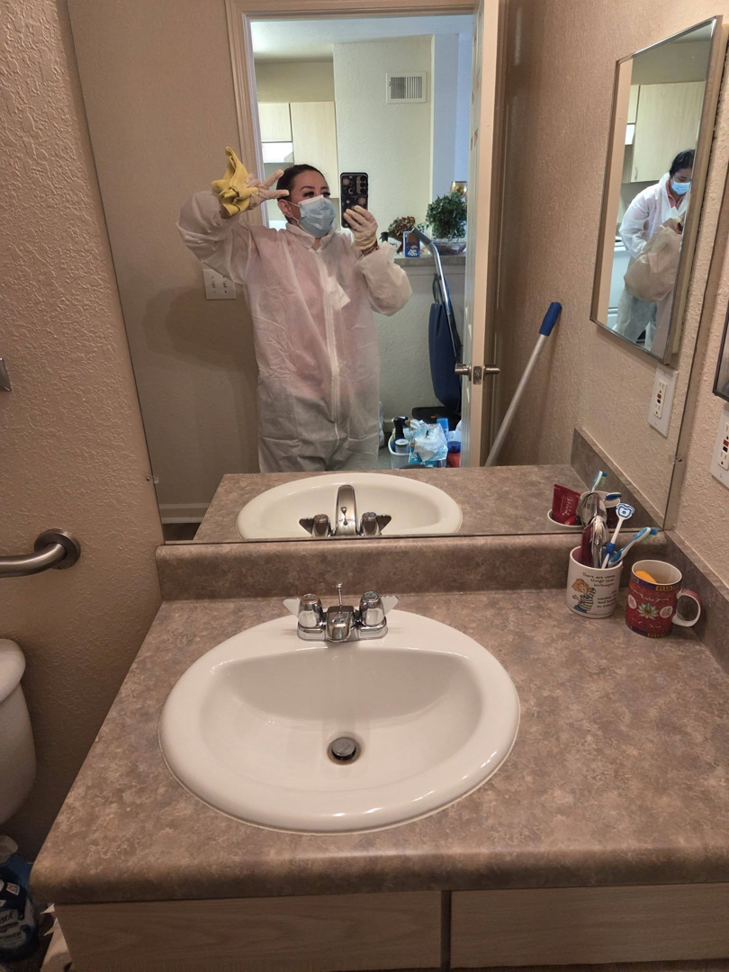 A house cleaner in uniform and mask taking a selfie in a clean bathroom at Expert Cleaners LLC in Jacksonville, FL.