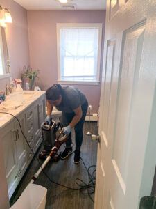 A professional house cleaner from So Clean Cleaning Services vacuuming a bathroom floor in a home in East Providence, RI.