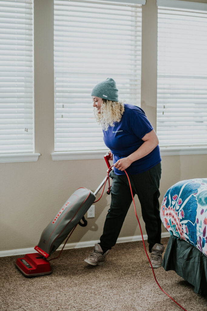 A house cleaner from Clean Queen House Cleaning vacuuming the carpet in a bedroom in Arvada, CO.