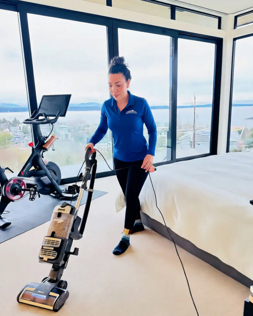 A house cleaner vacuuming a bedroom with a scenic view for Crest Cleaning Services in Auburn, WA