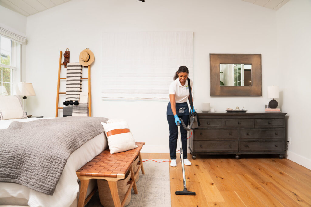A house cleaner from The Cleaning Authority - Bowie, MD, vacuuming a wooden floor in a spacious bedroom.