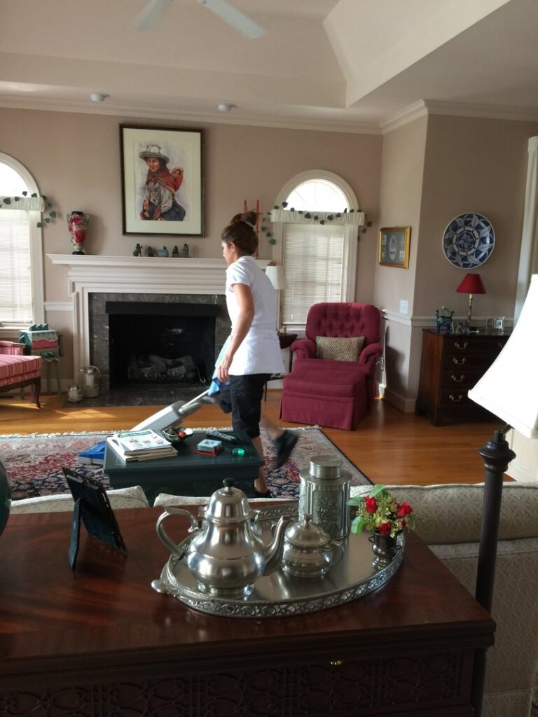 A house cleaner from Carolina Cleaning Services in Rocky Mount, NC, vacuuming a carpeted living room floor.