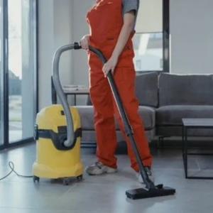 A house cleaner in orange overalls vacuuming a living room floor for Clean Home Nash in Nashville, TN.