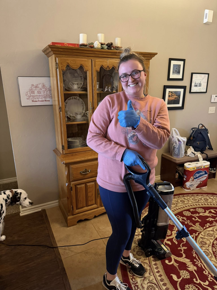 A house cleaner wearing gloves and vacuuming a living room, providing services for Hey Sis Cleaning LLC in Edmond, OK.