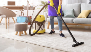 A house cleaner wearing yellow gloves vacuuming a white rug in a living room for PAP-Cleaning Services in Fort Lauderdale, FL.
