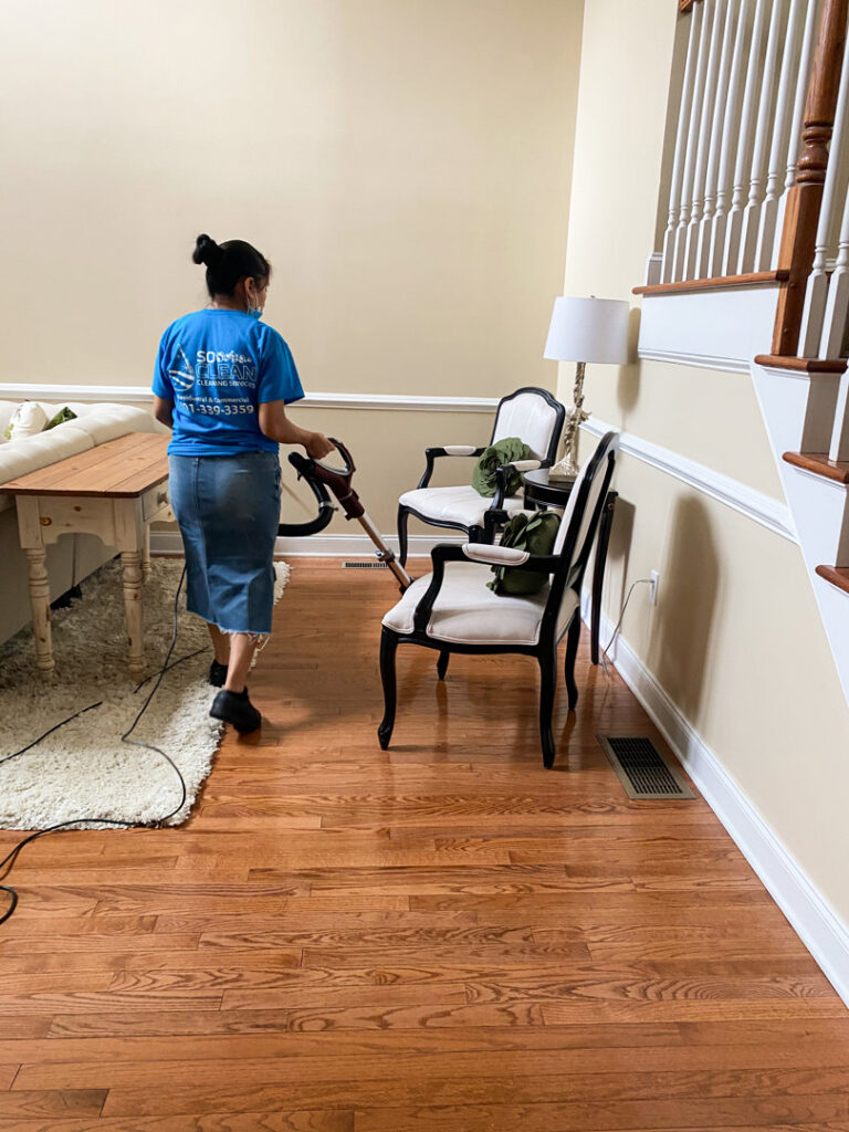 A house cleaner from So Clean Cleaning Services vacuuming a living room rug in a residence in East Providence, RI.