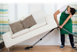 A house cleaner vacuuming under a sofa in a home by Doozy Cleaning Services in Denver, CO.