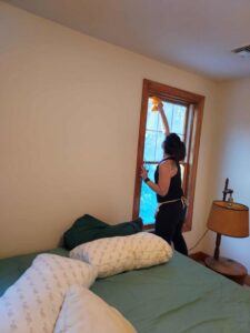 A house cleaner from KDG Decluttering washing a bedroom window in a home in Manchester, NH.