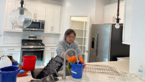 A house cleaner from House Cleaning Solutions in Mesa, AZ, is washing kitchen items in a kitchen sink.