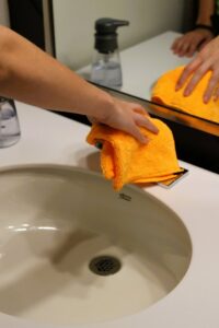 A professional house cleaner wiping down a bathroom sink with an orange microfiber cloth for Natural Clean in Sioux Falls, SD.