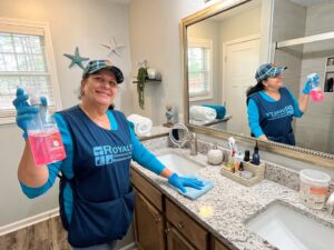 A house cleaner from Royalty Commercial & Residential Cleaning LLC wiping a bathroom vanity in a residential home in Sumter, SC.