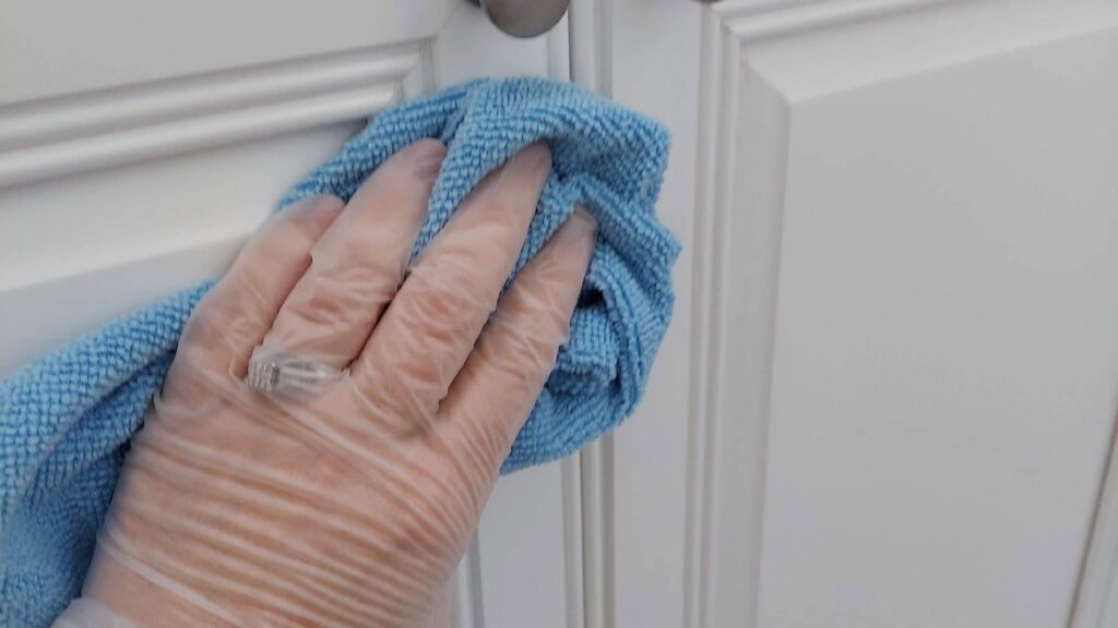 A house cleaner's gloved hand wiping a white kitchen cabinet with a blue cloth for Maid For You Cleaning & Organizing in Peoria, IL.