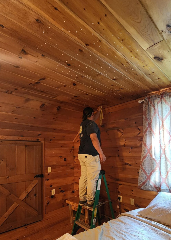 A house cleaner from Brighter Days Cleaning wiping down a wooden ceiling in a bedroom in Sacramento, CA