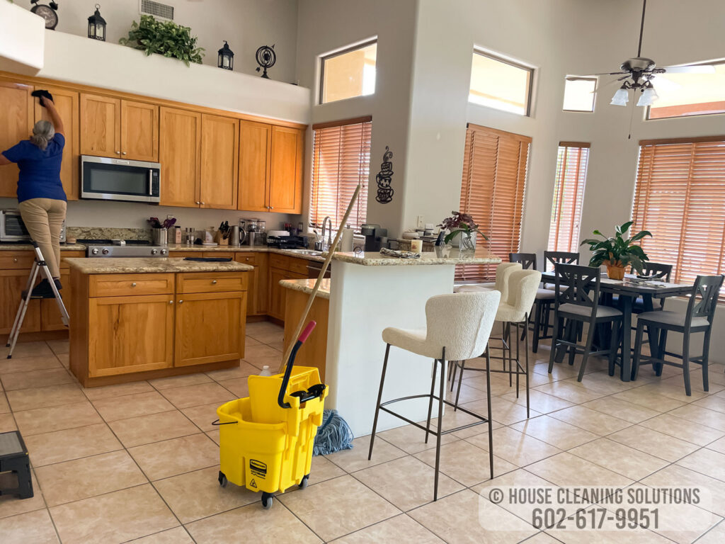 A house cleaner from House Cleaning Solutions in Mesa, AZ, is wiping down kitchen cabinets from a step ladder.