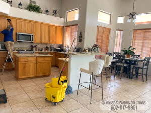 A house cleaner from House Cleaning Solutions in Mesa, AZ, is wiping down kitchen cabinets from a step ladder.