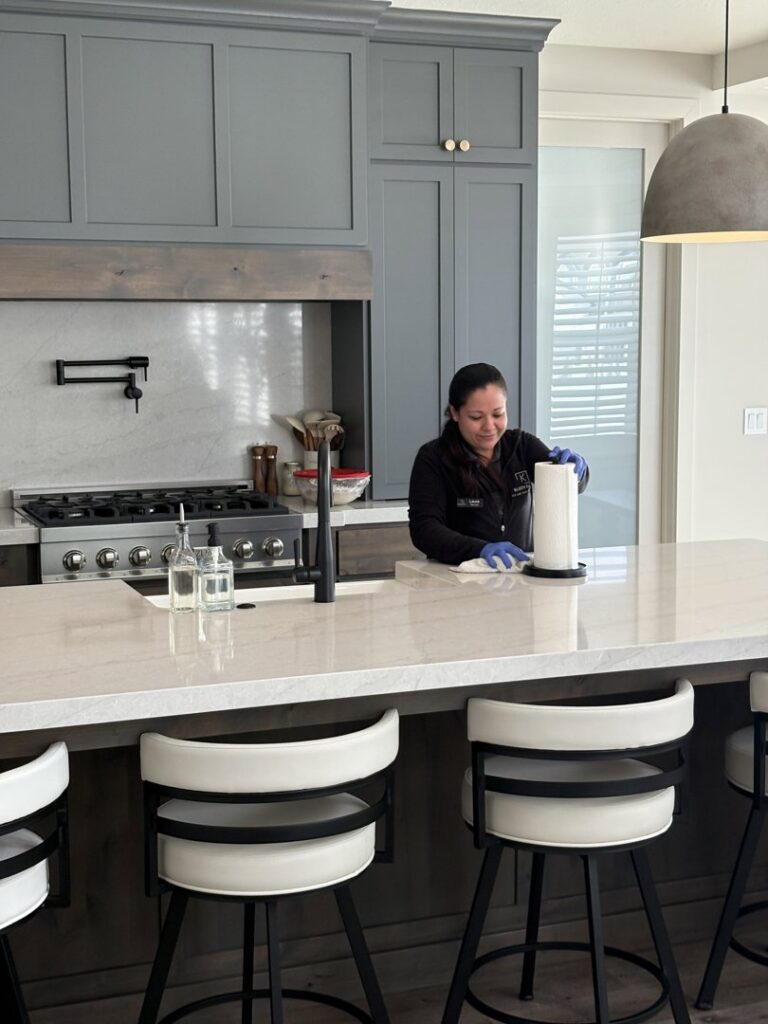 A Kleen Slate house cleaner wearing blue gloves, wiping down a large kitchen island with a paper towel in Shakopee, MN.