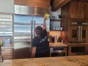 A professional house cleaner from ECO Friends cleaning service wiping down a stainless steel refrigerator in a kitchen in Carson City, NV.