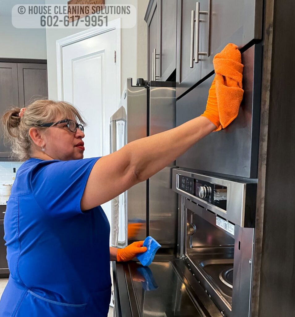 A house cleaner from House Cleaning Solutions in Mesa, AZ, is wiping down a stainless steel refrigerator.