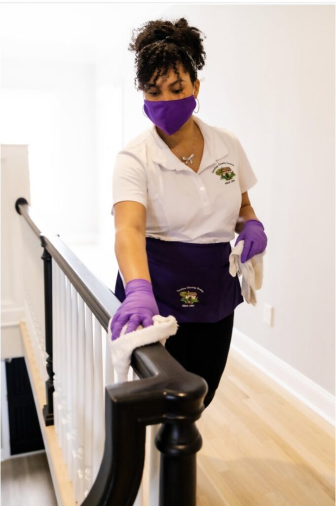A house cleaner from Carolina Cleaning Services in Rocky Mount, NC, wiping a dark wooden stair railing.