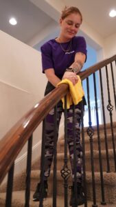 A house cleaner from Clean Queen House Cleaning wiping down a wooden stair railing in Arvada, CO.