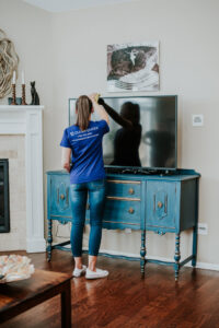 A house cleaner from Clean Queen House Cleaning carefully wiping a television screen in a living room in Arvada, CO.