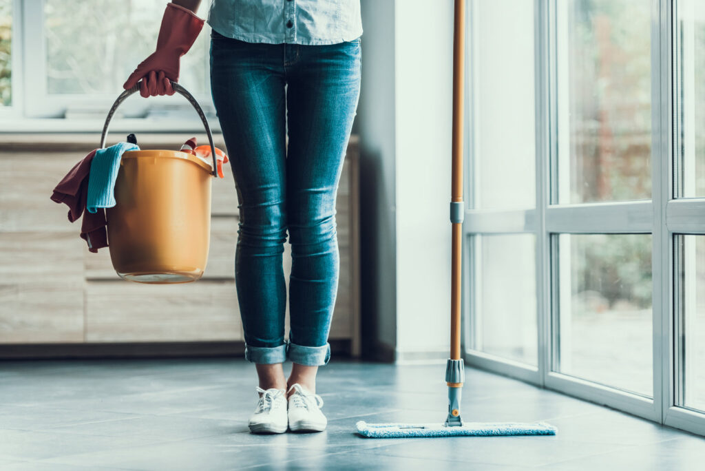 A house cleaner wearing gloves, holding a bucket of supplies and standing next to a mop, from Christina's Tidy Homes in Canton, OH.