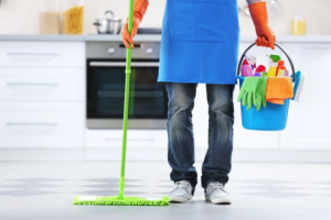 A house cleaner standing in a kitchen with a mop and a bucket of supplies for Price Cleaning Services Omaha in Council Bluffs, IA.
