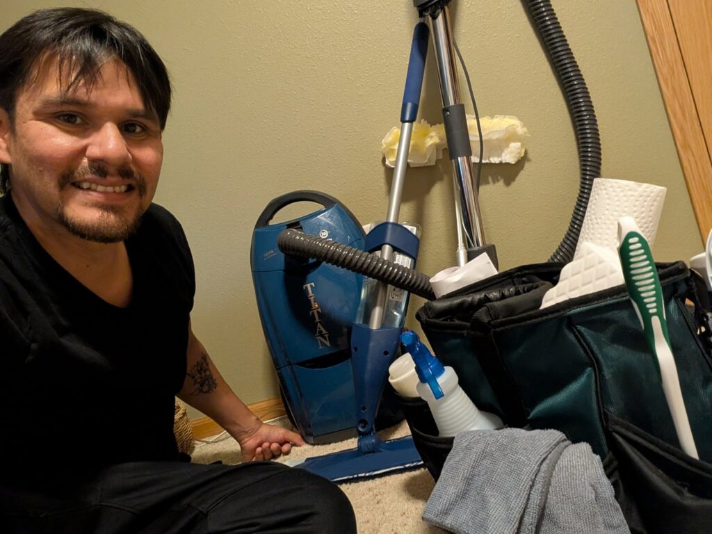 A house cleaner smiling next to a caddy full of cleaning supplies and a vacuum from Clean and Pristine Solutions in Fargo, ND.