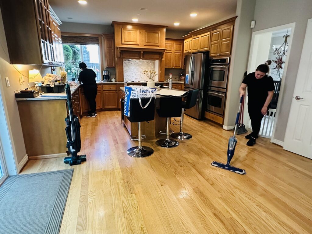 House cleaners mopping a hardwood floor and wiping counters in a kitchen with wooden cabinets, provided by Quesada's cleaning services llc in Seattle, WA.