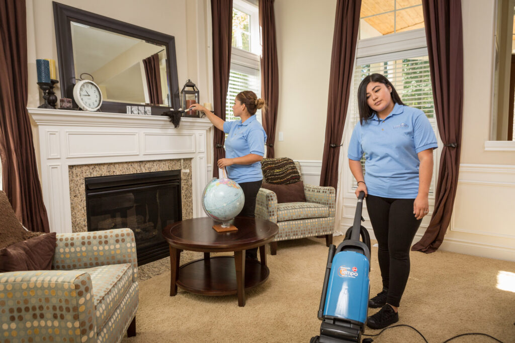 Two house cleaners vacuuming and dusting a living room for Crest Cleaning Services in Auburn, WA