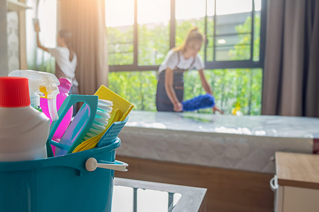 Cleaning supplies in the foreground with two cleaners working in a home, provided by Harsh's Cleaning Services LLC in Canton, OH.