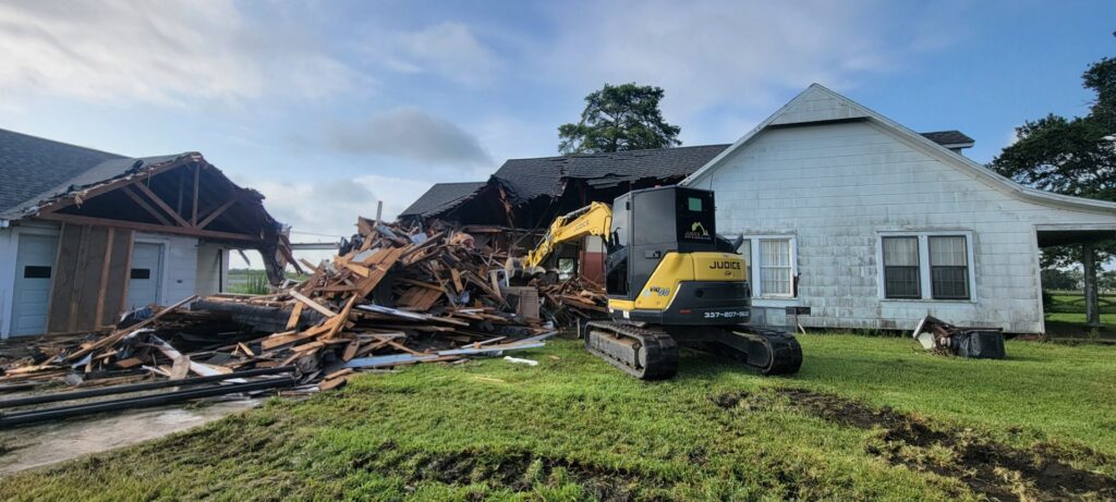 An excavator from Judice Dirt & Demolition actively demolishing a house, with a large pile of debris in Lafayette, LA.