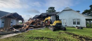 An excavator from Judice Dirt & Demolition actively demolishing a house, with a large pile of debris in Lafayette, LA.