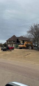 An excavator actively demolishing a house, showcasing demolition services by East Shelby Demolition & Pool Removal in Olive Branch, MS.