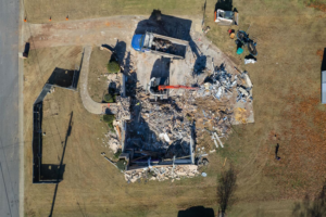 Aerial view of a house demolition site with an excavator and dump truck, handled by Nuckles Services in Birmingham, AL