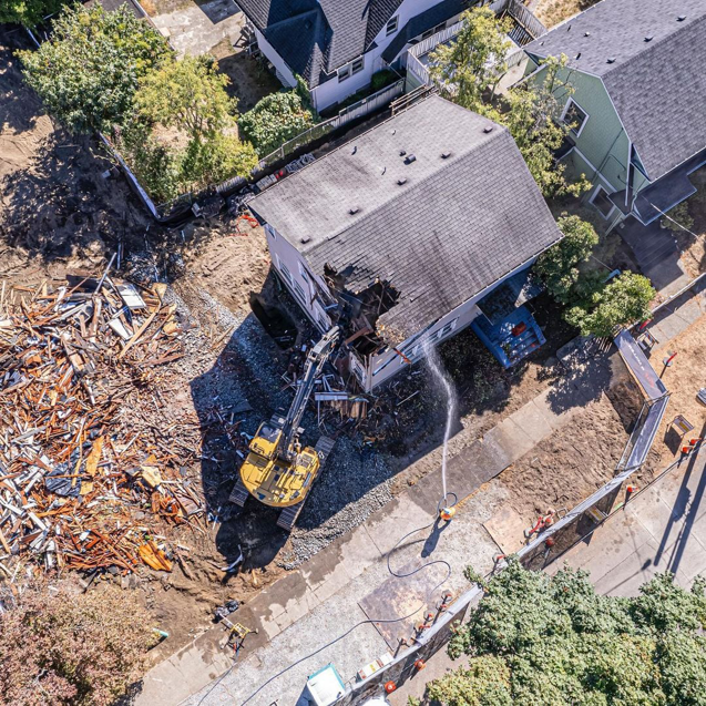 A house undergoing demolition with an excavator and dust control measures, performed by Rainstate Earthworks in Auburn, WA.