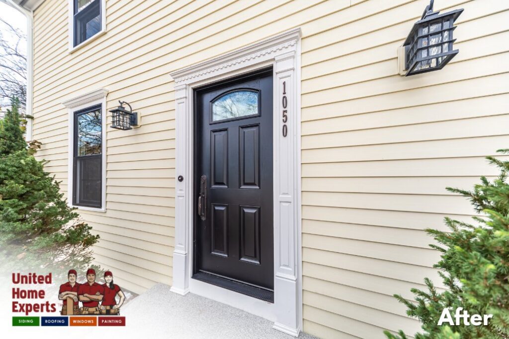 A close-up of a house entrance featuring new light yellow siding and a black door, completed by United Home Experts in Ashland, MA