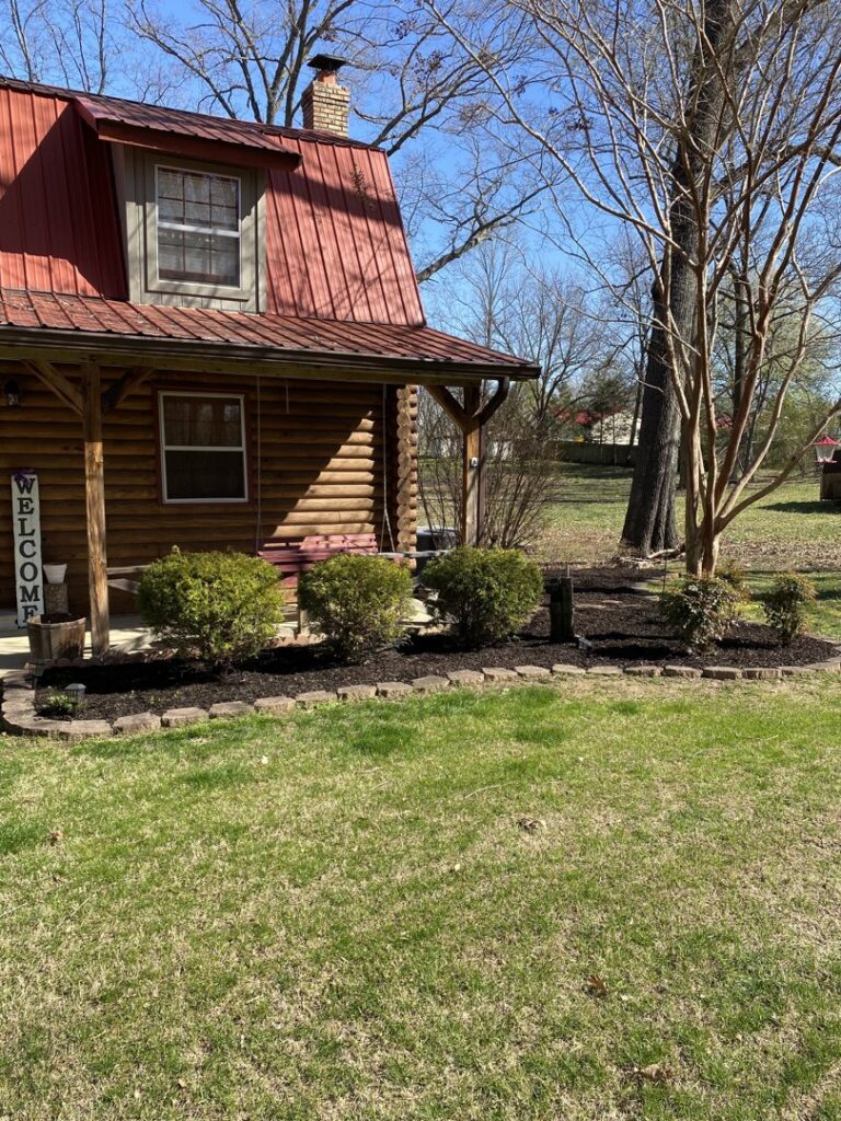 The front of a house featuring dark mulched garden beds with various healthy bushes by The Otherside Lawn Solutions in Ankeny, IA.